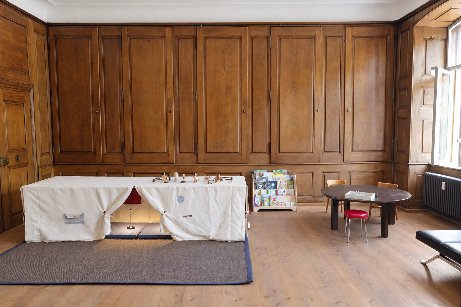 Wood-panelled Lernbus room with a fabric play den, books and a round table with children's chairs.